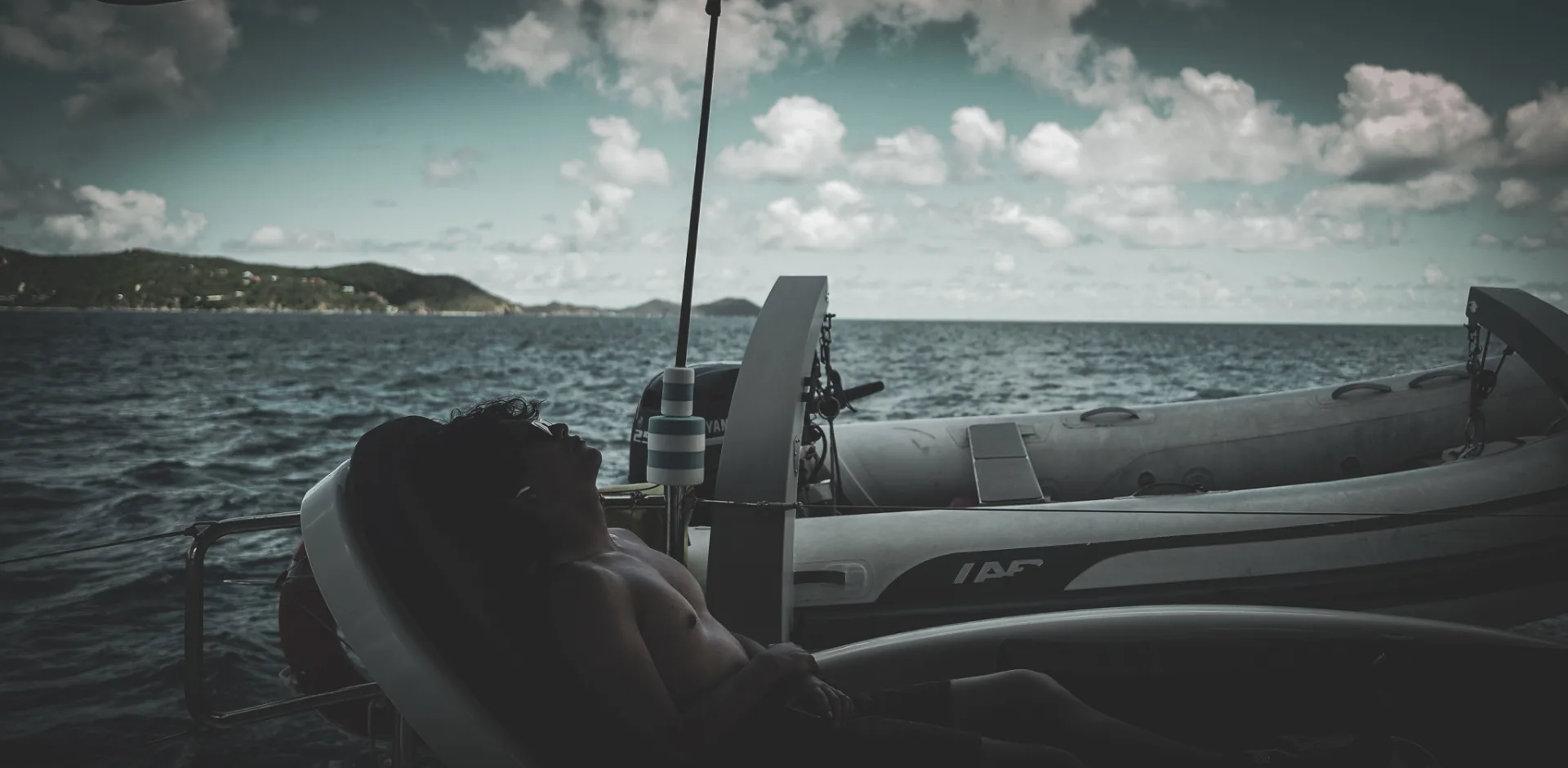 Guest sunbathing on the aft sun pad with the dinghy and St. John shoreline behind