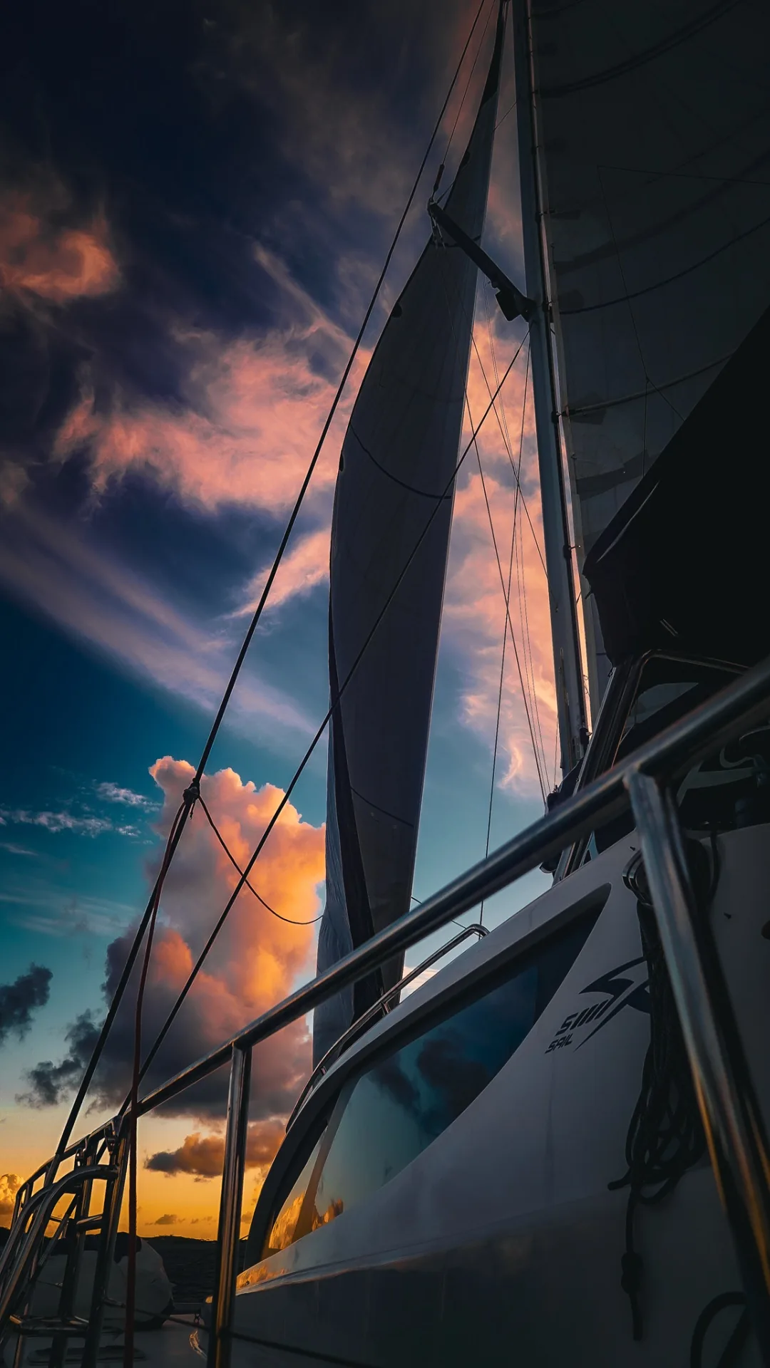 Mainsail and genoa filled with wind under a pink and gold Caribbean sunset aboard Stella Blue