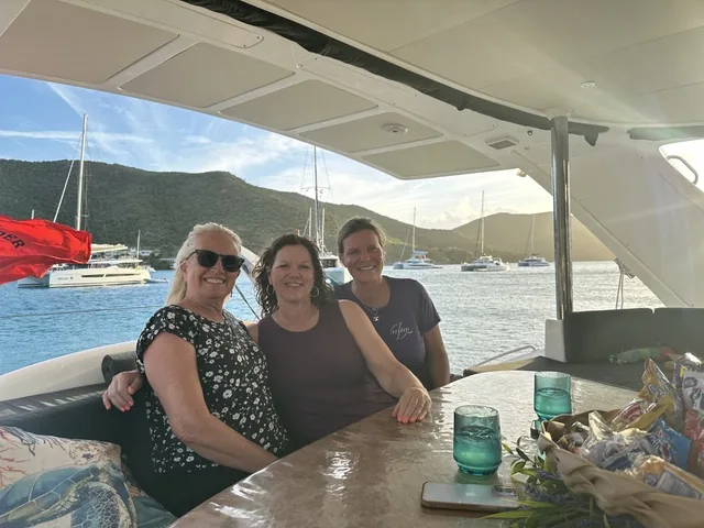 Three guests laughing in the cockpit of Stella Blue with a Virgin Islands anchorage and catamarans behind