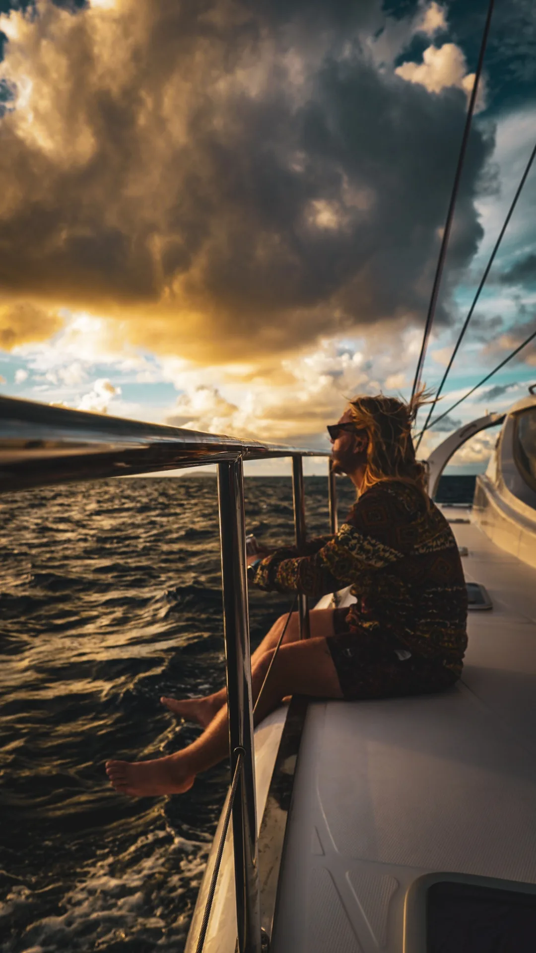 Guest sitting on the side deck of Stella Blue at sunset, feet dangling above the water in the USVI