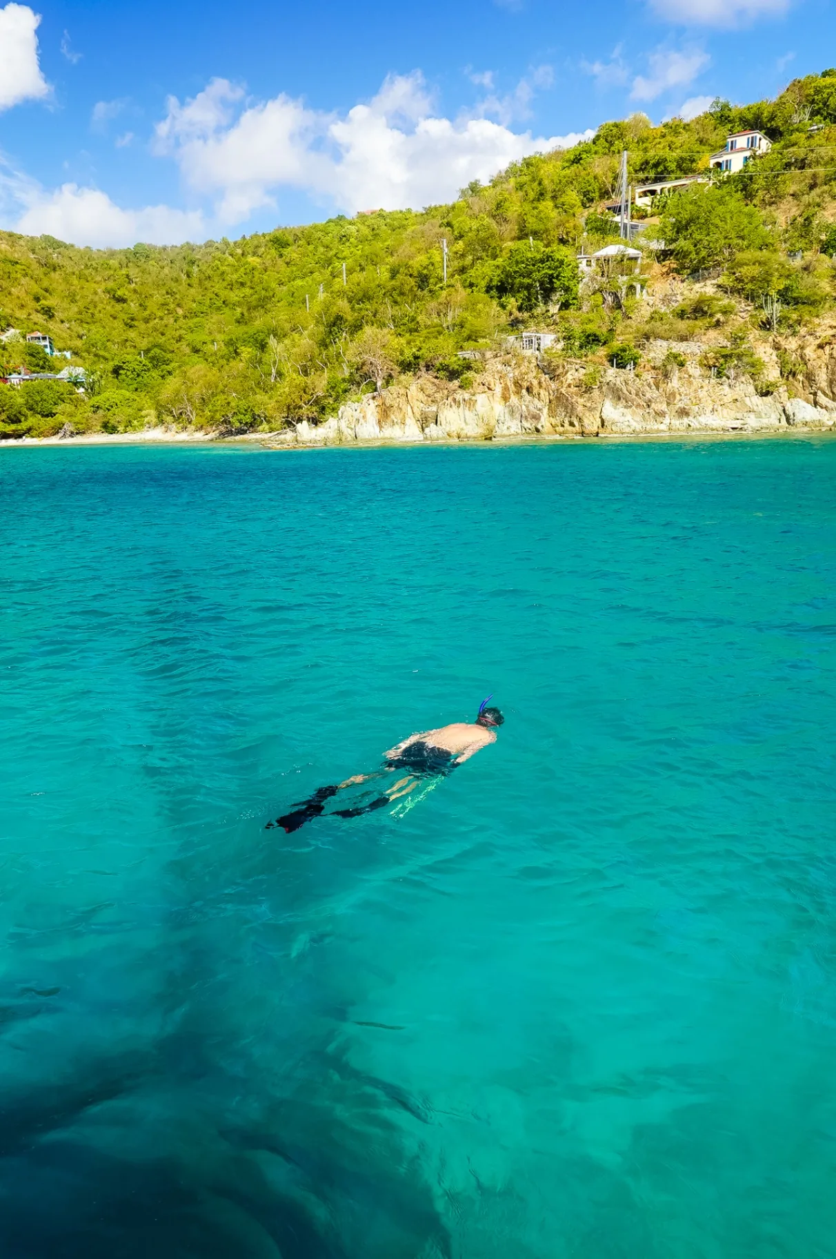 Guest snorkeling in clear turquoise water below a green St. John hillside