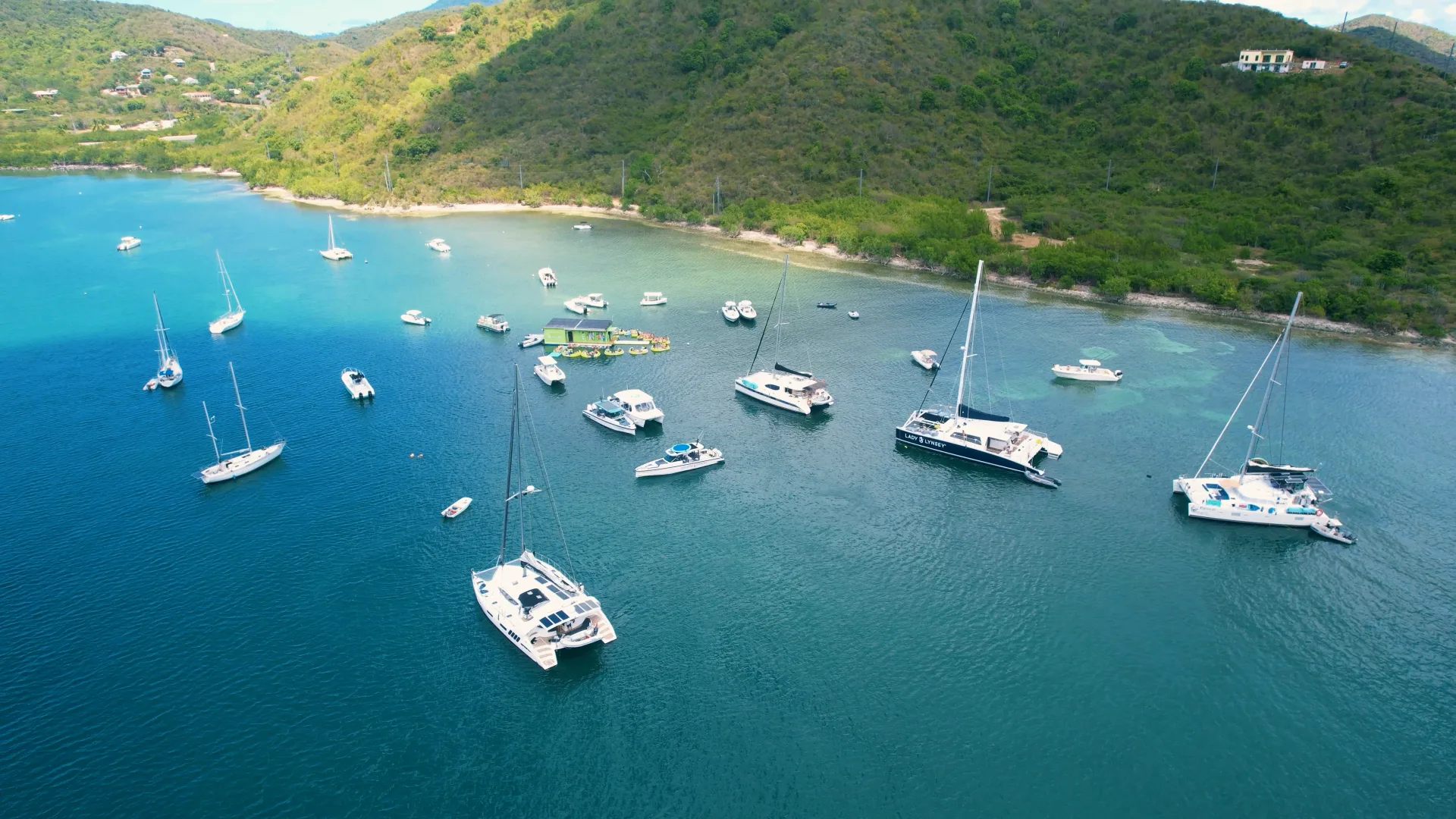 Aerial view of a Virgin Islands anchorage filled with sailboats and catamarans beside a lush green hillside