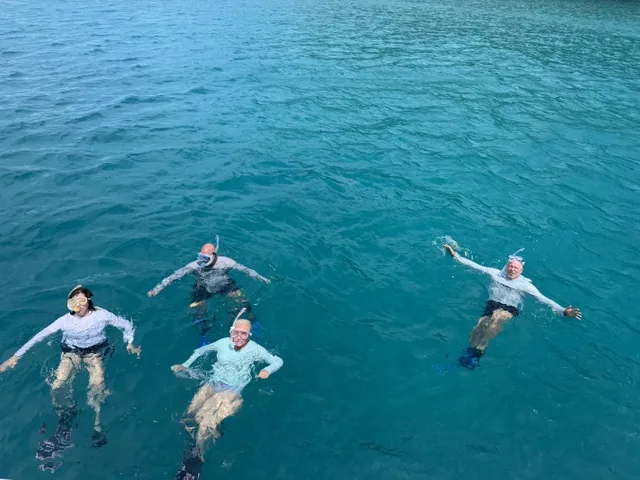 Four guests floating and snorkeling in turquoise Virgin Islands water beside Stella Blue catamaran