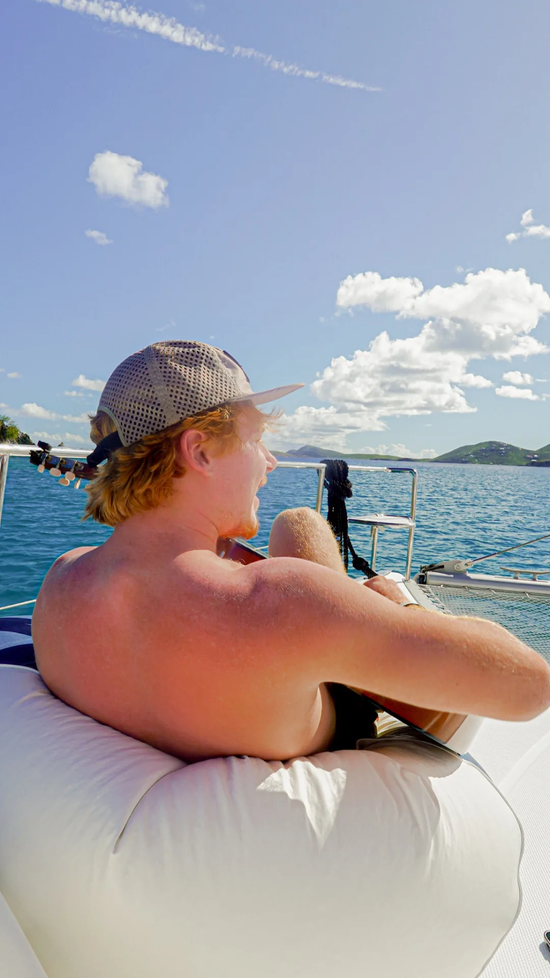 Guest playing acoustic guitar on the bow trampoline of Stella Blue with Virgin Islands in the distance