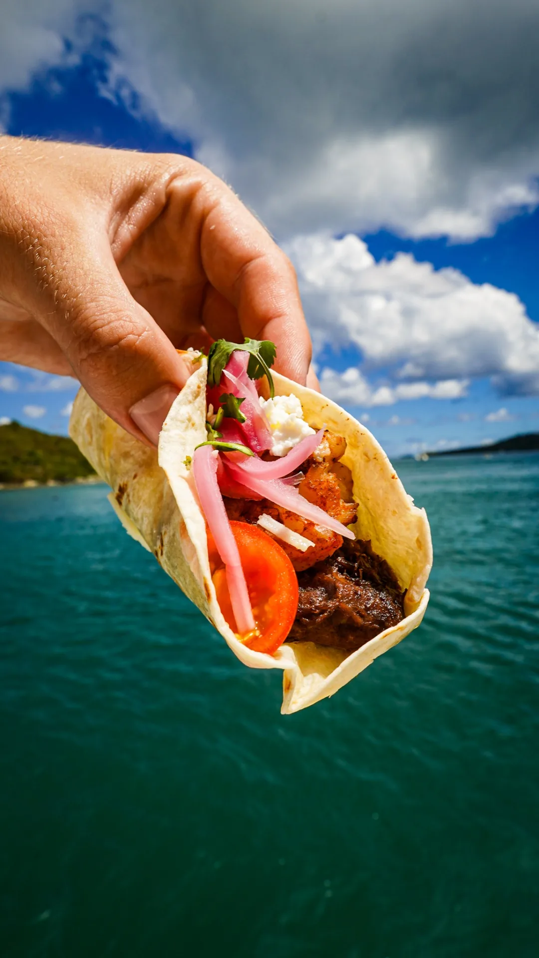 Fresh shrimp and short rib taco held above turquoise USVI water aboard Stella Blue