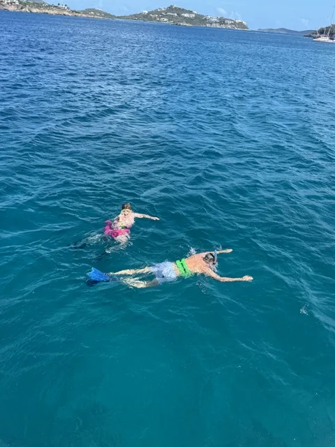 Two guests snorkeling in clear turquoise water beside Stella Blue with St. John shoreline in the distance