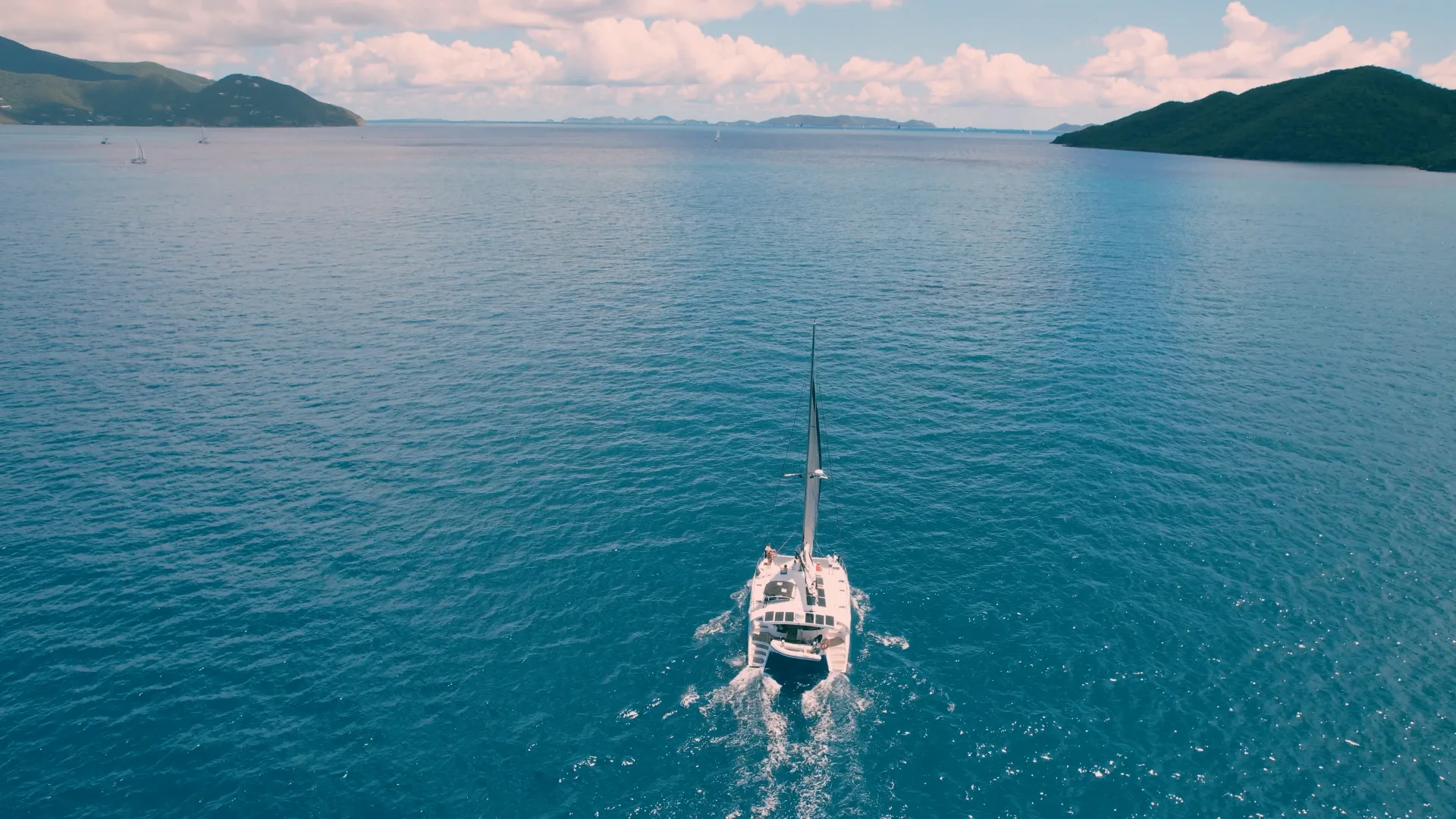Aerial view of Stella Blue catamaran sailing across deep blue Caribbean water with distant Virgin Islands on the horizon
