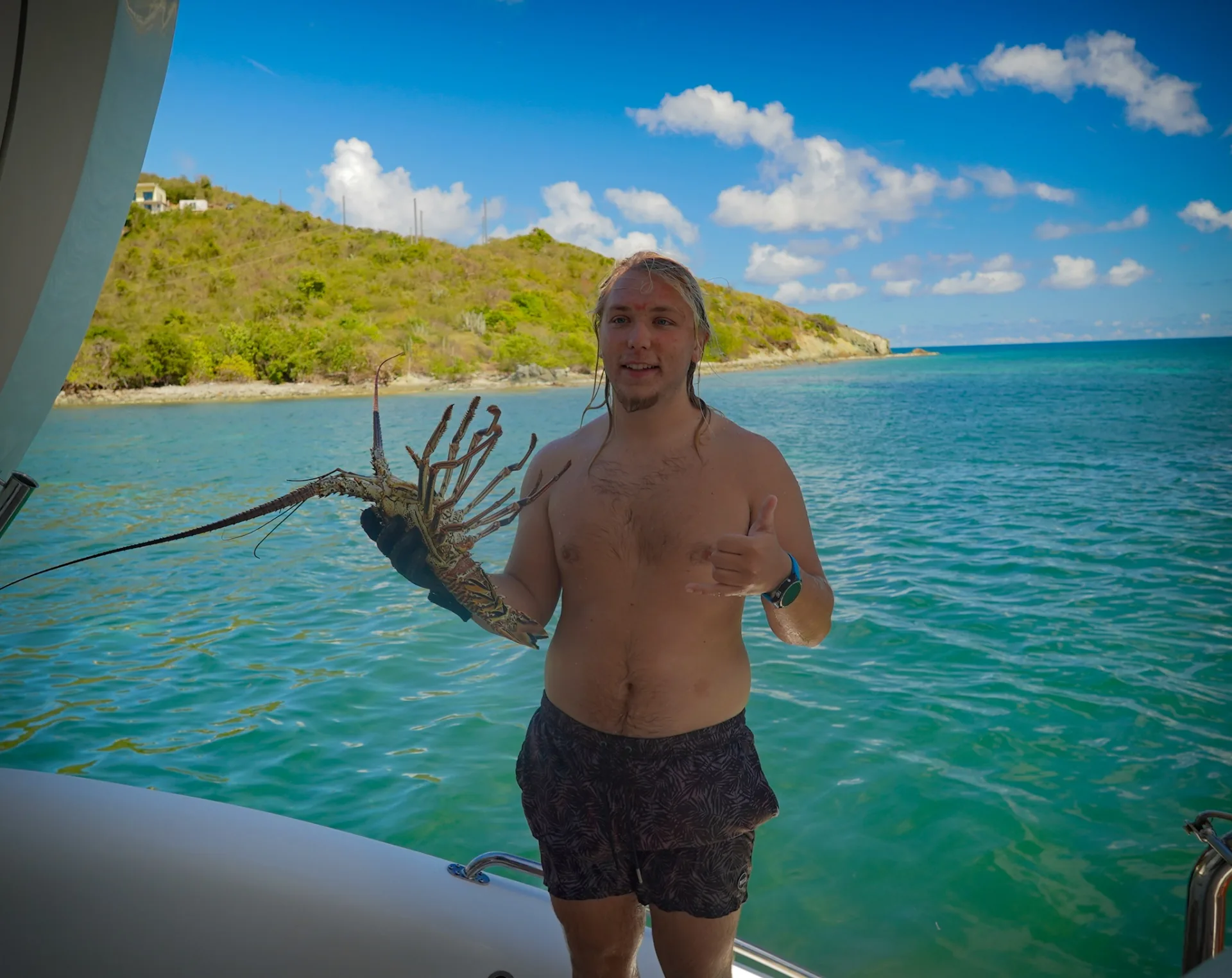 Guest on the swim platform giving a shaka and holding a fresh Caribbean spiny lobster