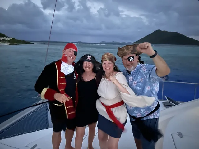 Four guests in pirate costumes laughing on the aft deck of Stella Blue at dusk in the Virgin Islands
