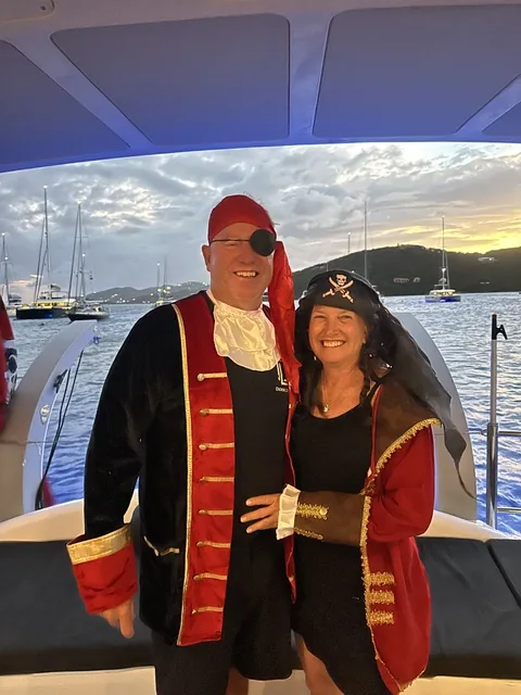 Two guests in pirate costumes posing on Stella Blue at sunset with the USVI anchorage behind them